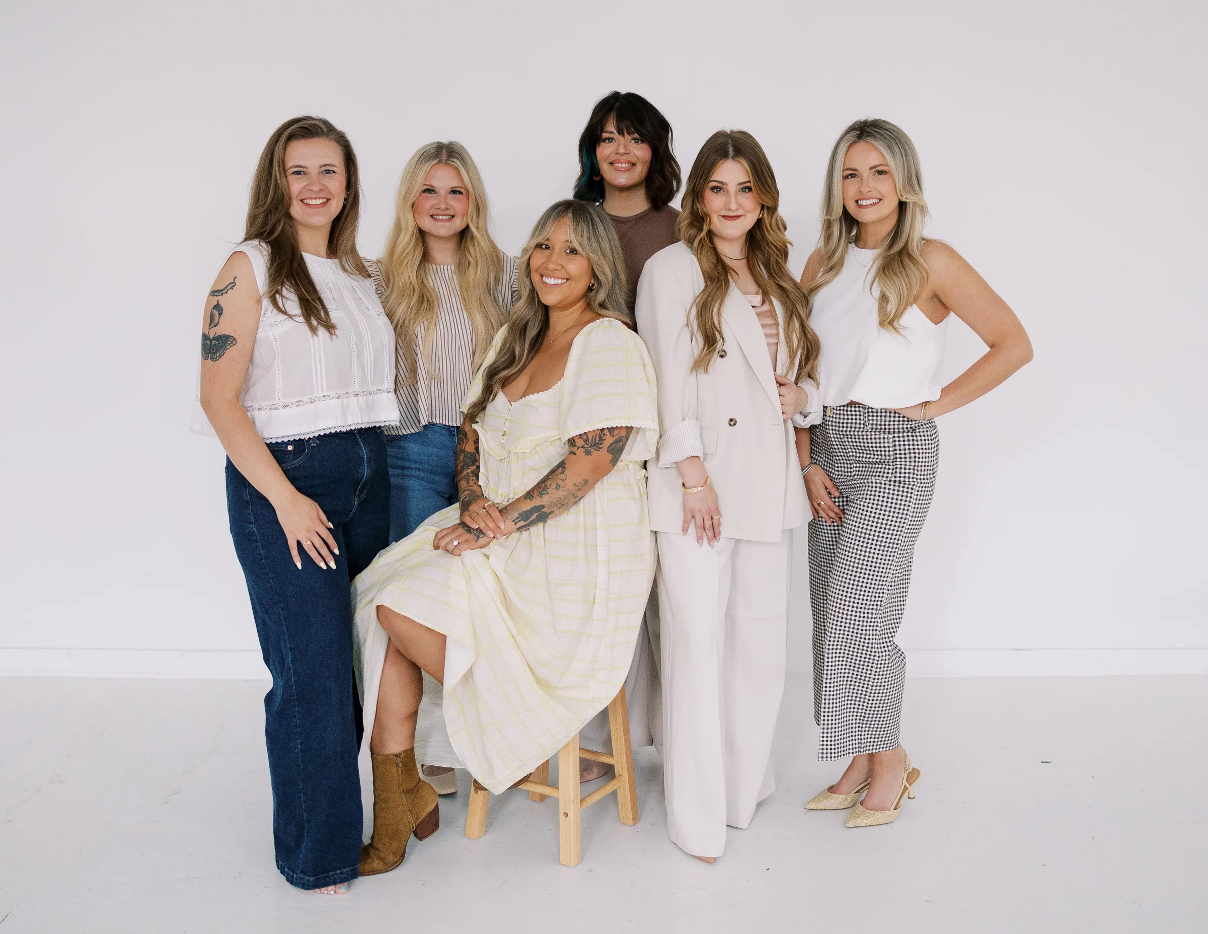 A warm, laughing group of Salon Joy stylists leaning together against a plain studio backdrop